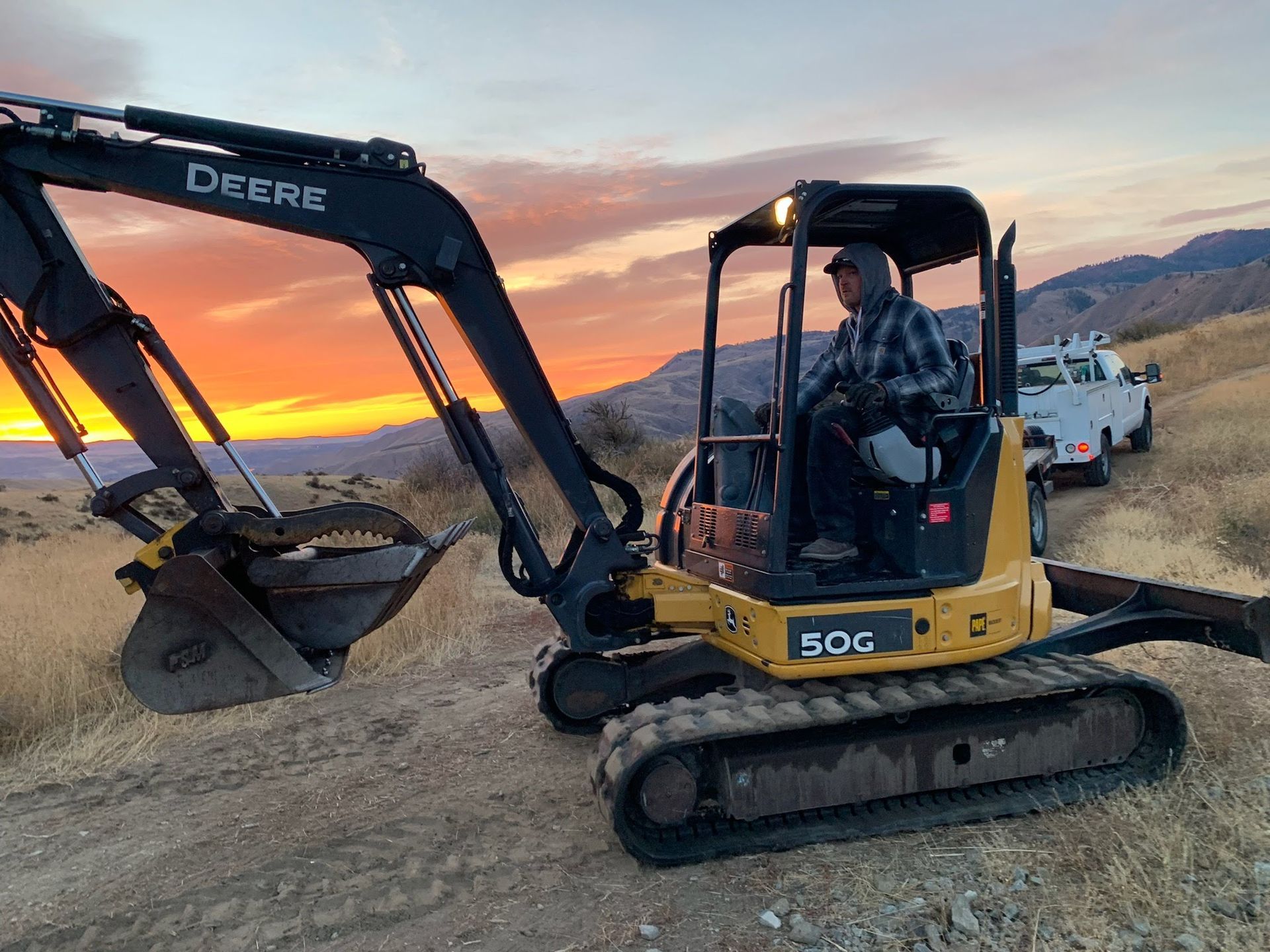 A man is driving a deere excavator on a dirt road.