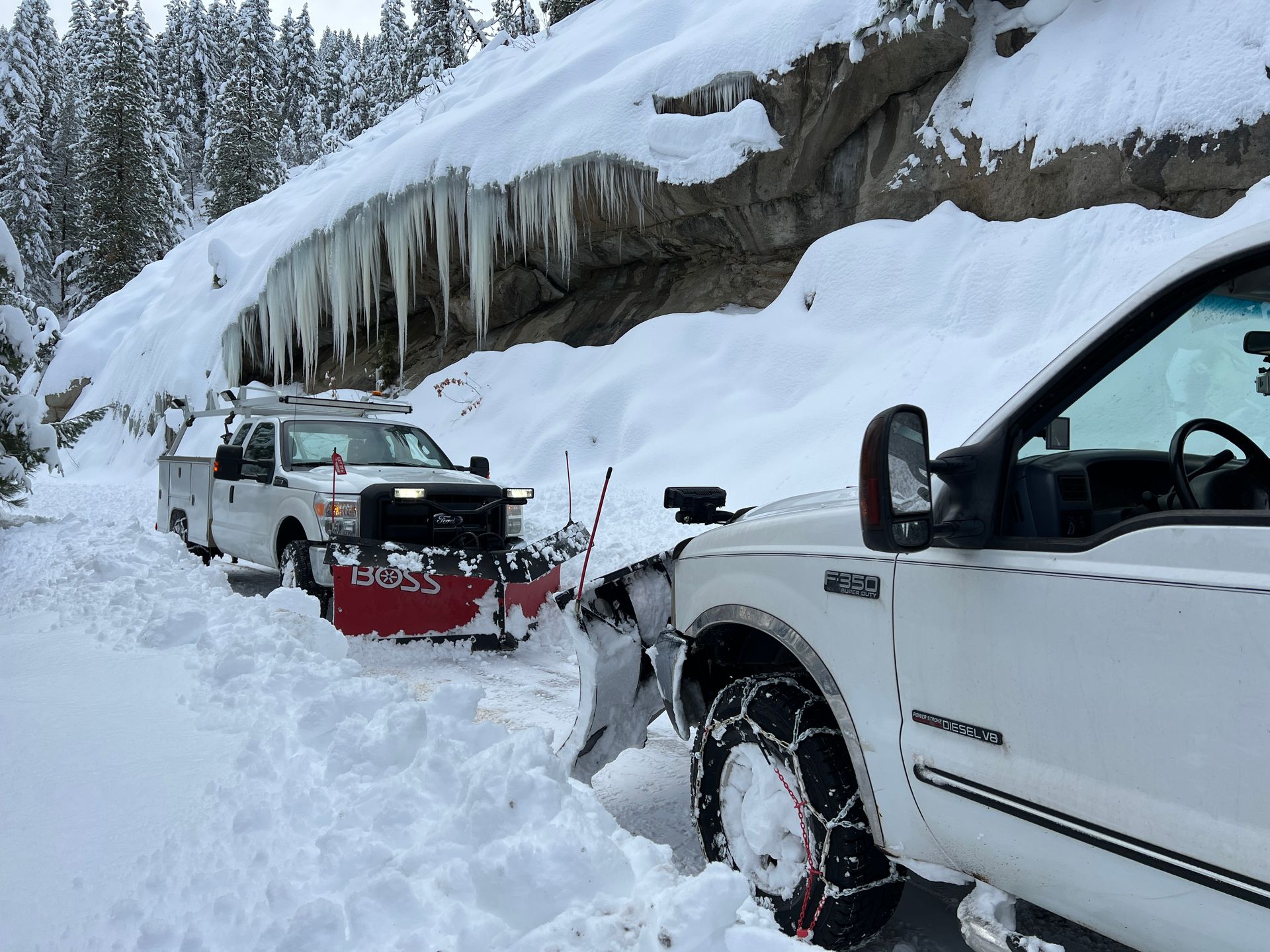 A white truck is parked in the snow next to a snow plow