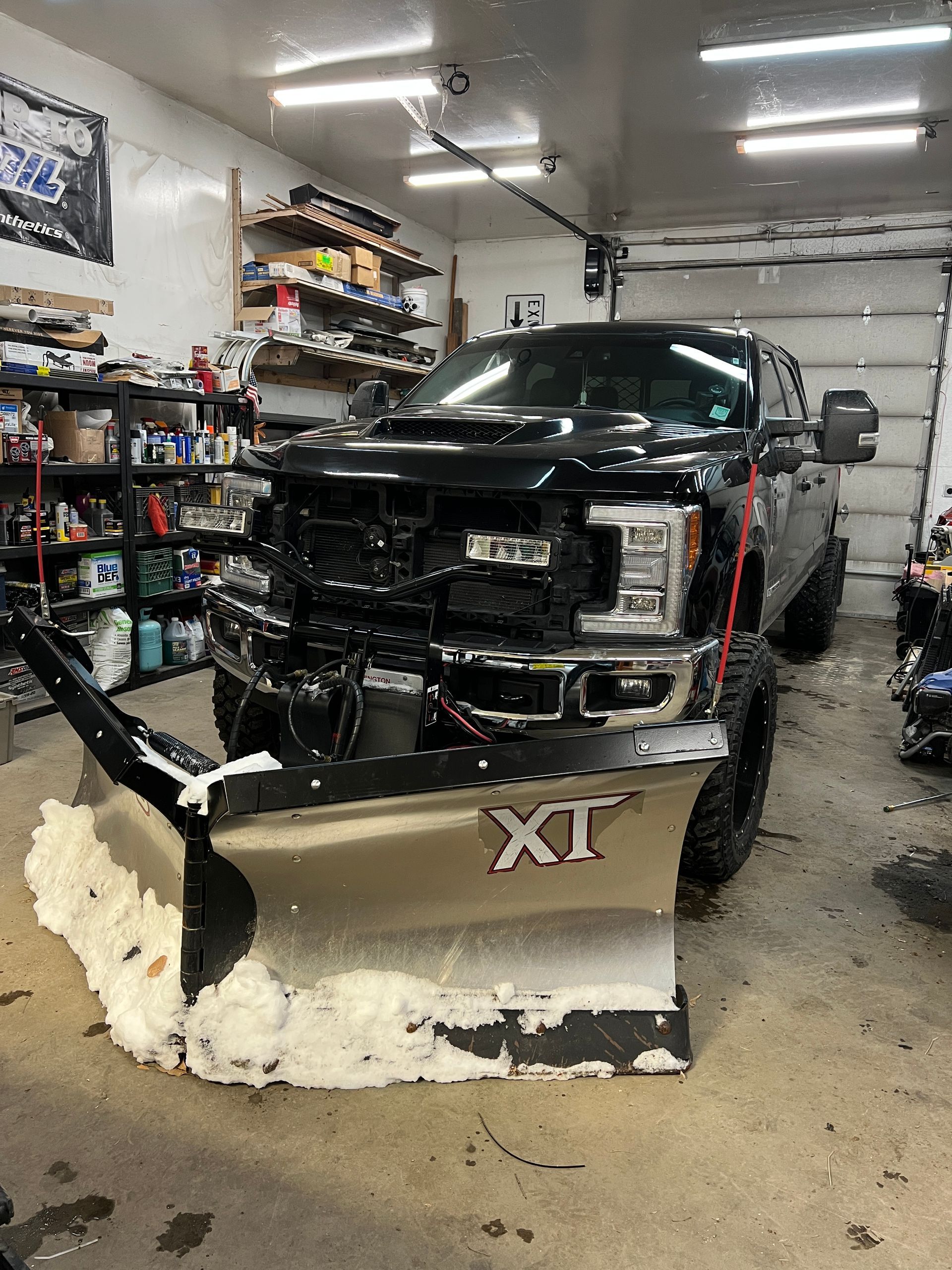 A truck with a snow plow attached to it is parked in a garage.
