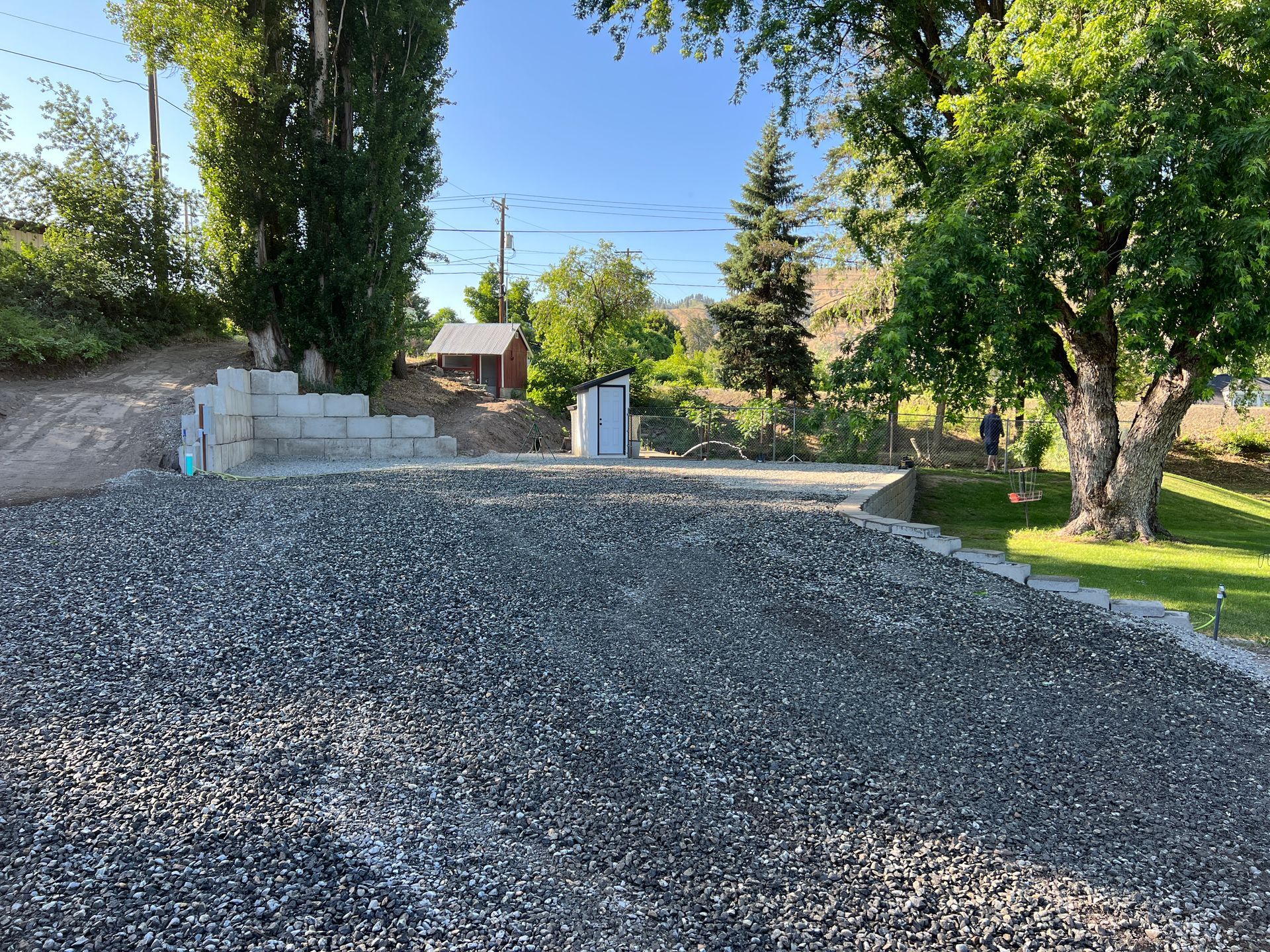 A gravel driveway with trees in the background and a house in the background.