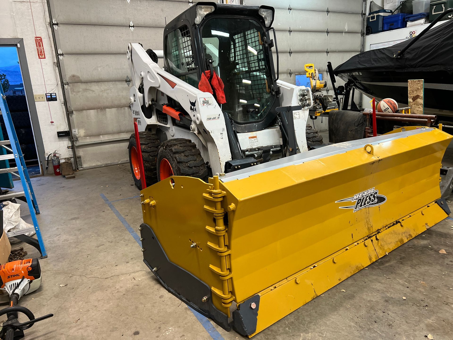 A snow plow is sitting in a garage next to a bulldozer.