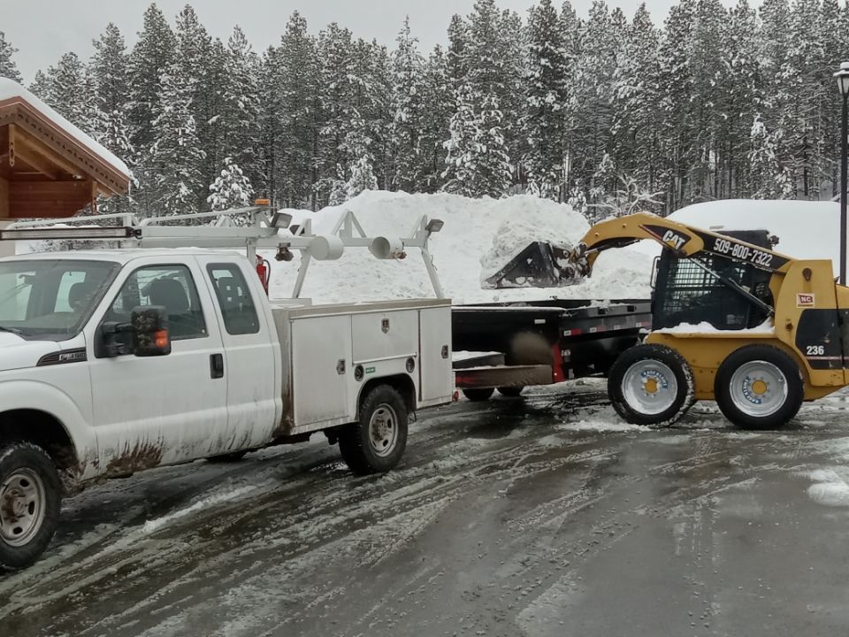 A white truck is being towed by a yellow skid steer