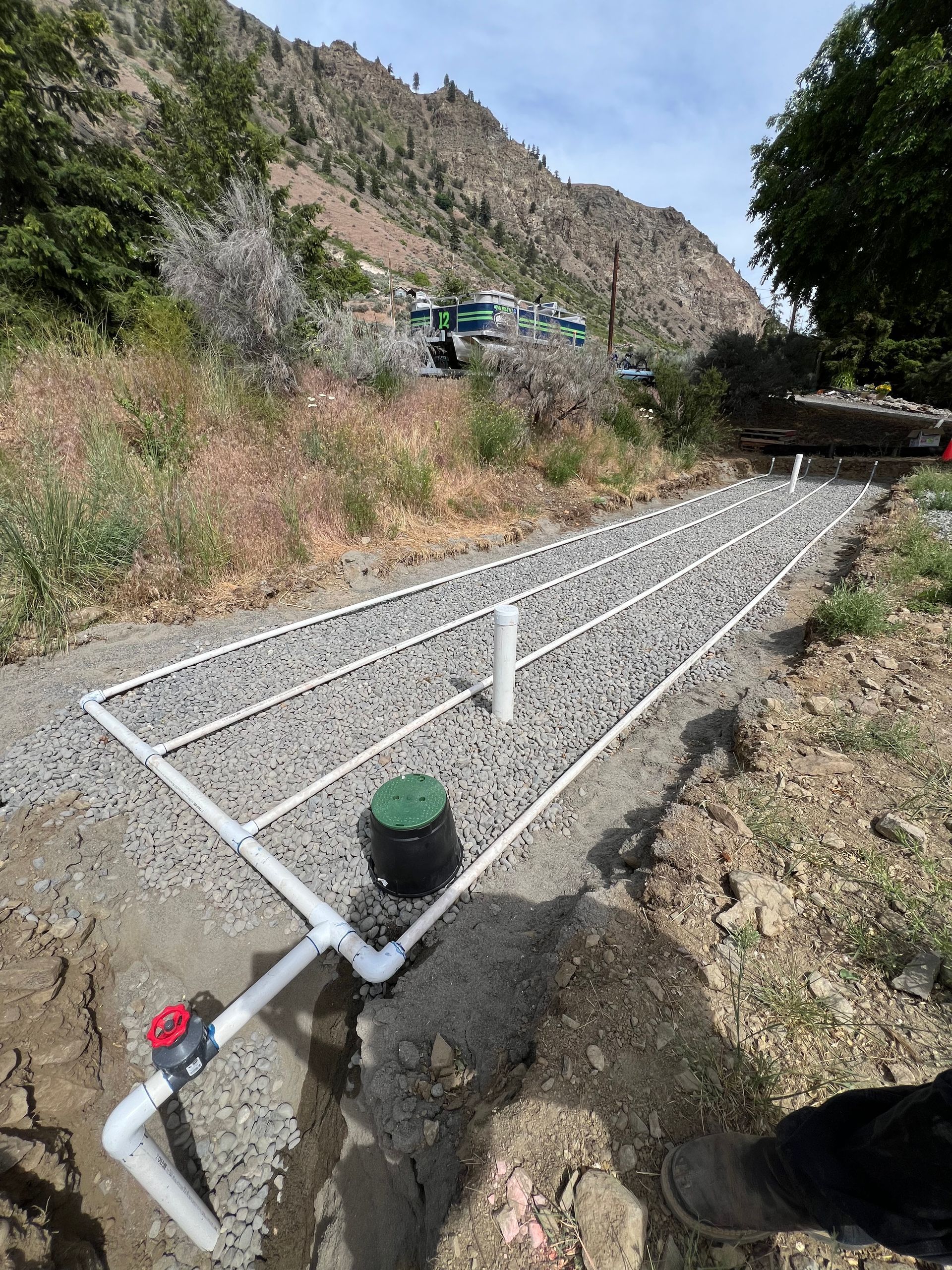 A person is standing in the dirt next to a drainage system.