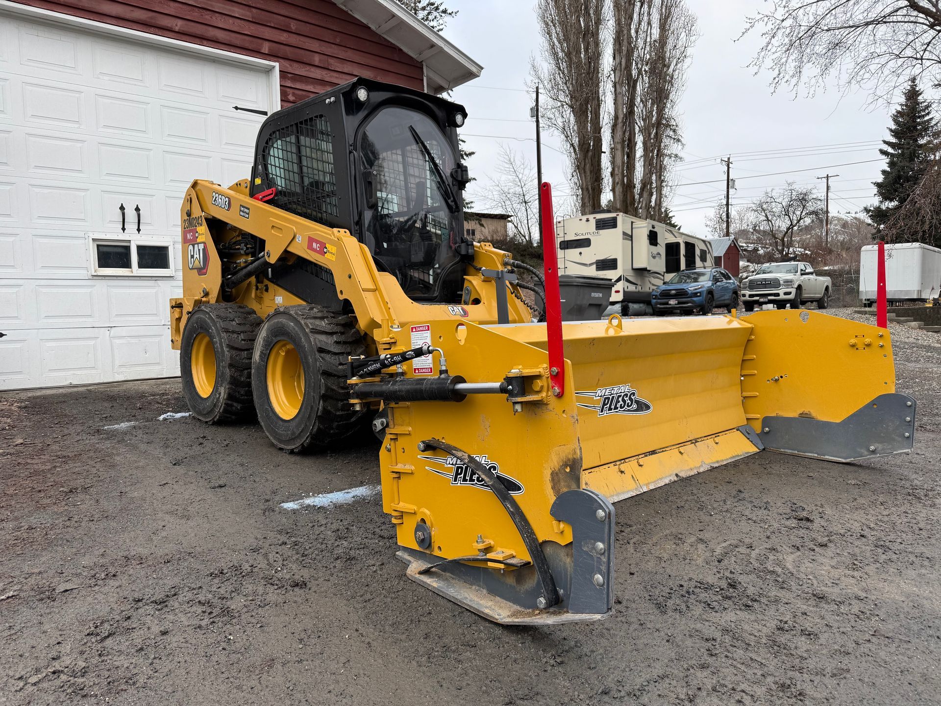 A yellow snow plow is parked in front of a garage.