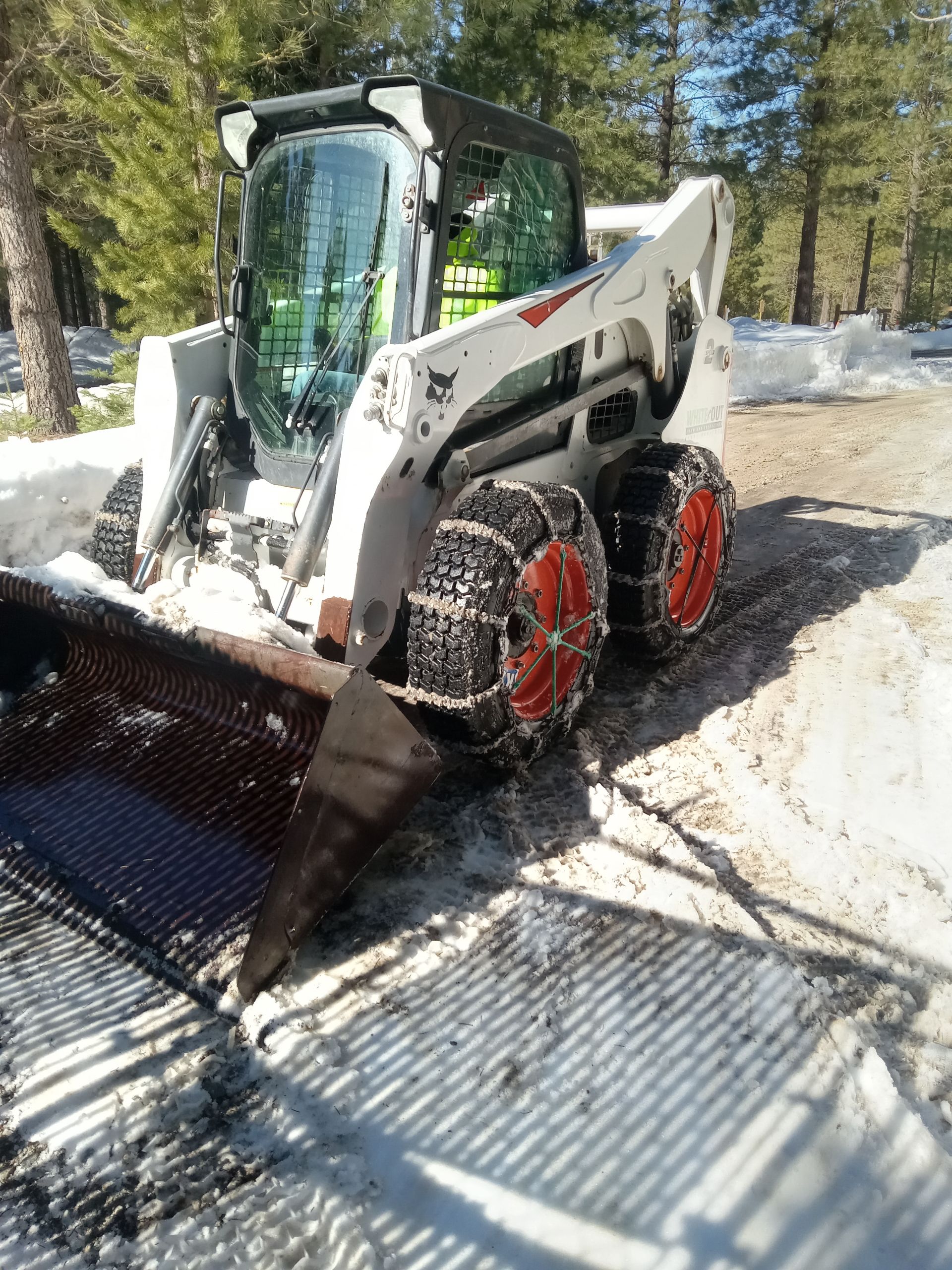 A bobcat snow plow is clearing snow from a road.