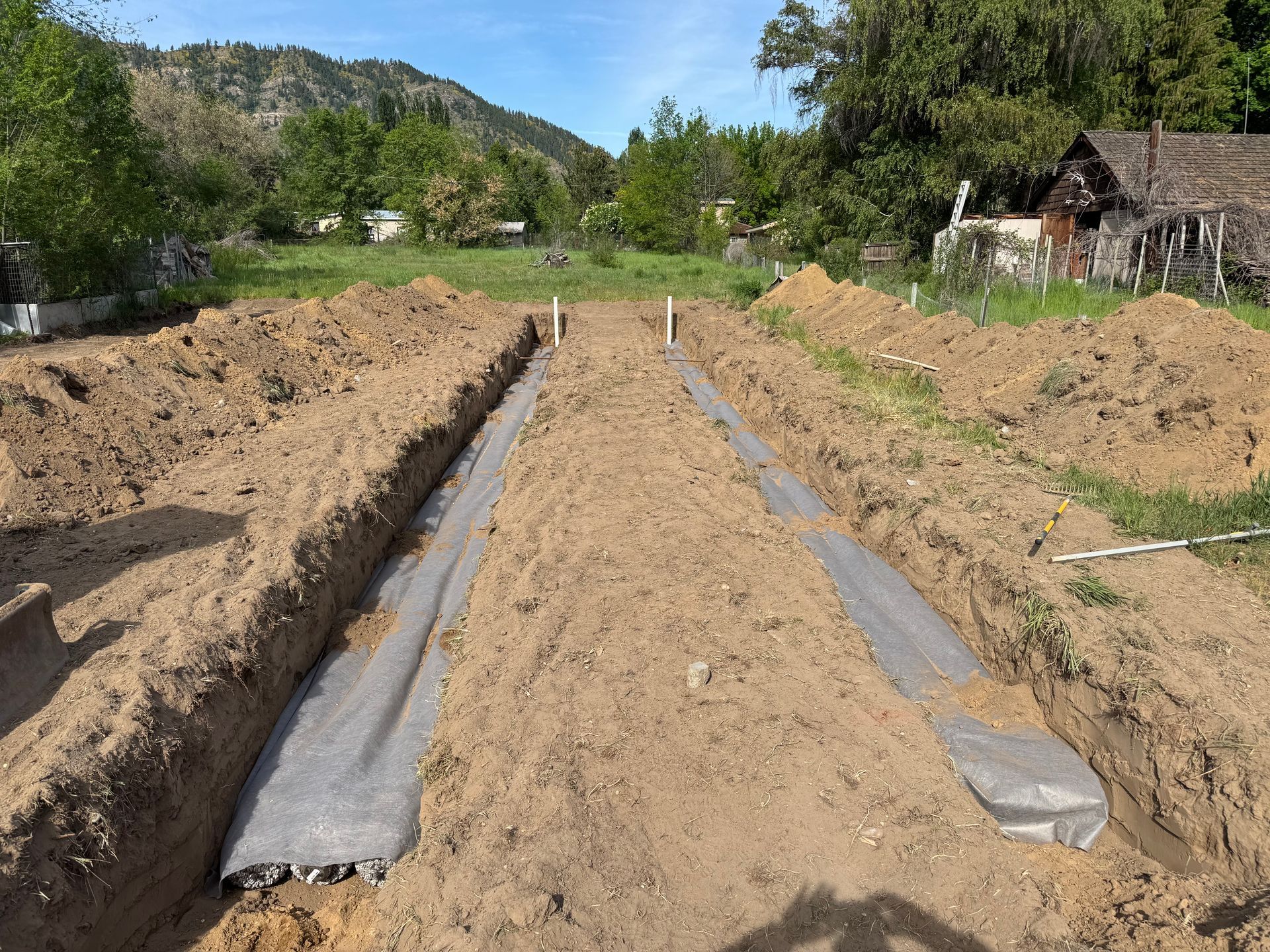 A dirt road is being built in a field with a house in the background.