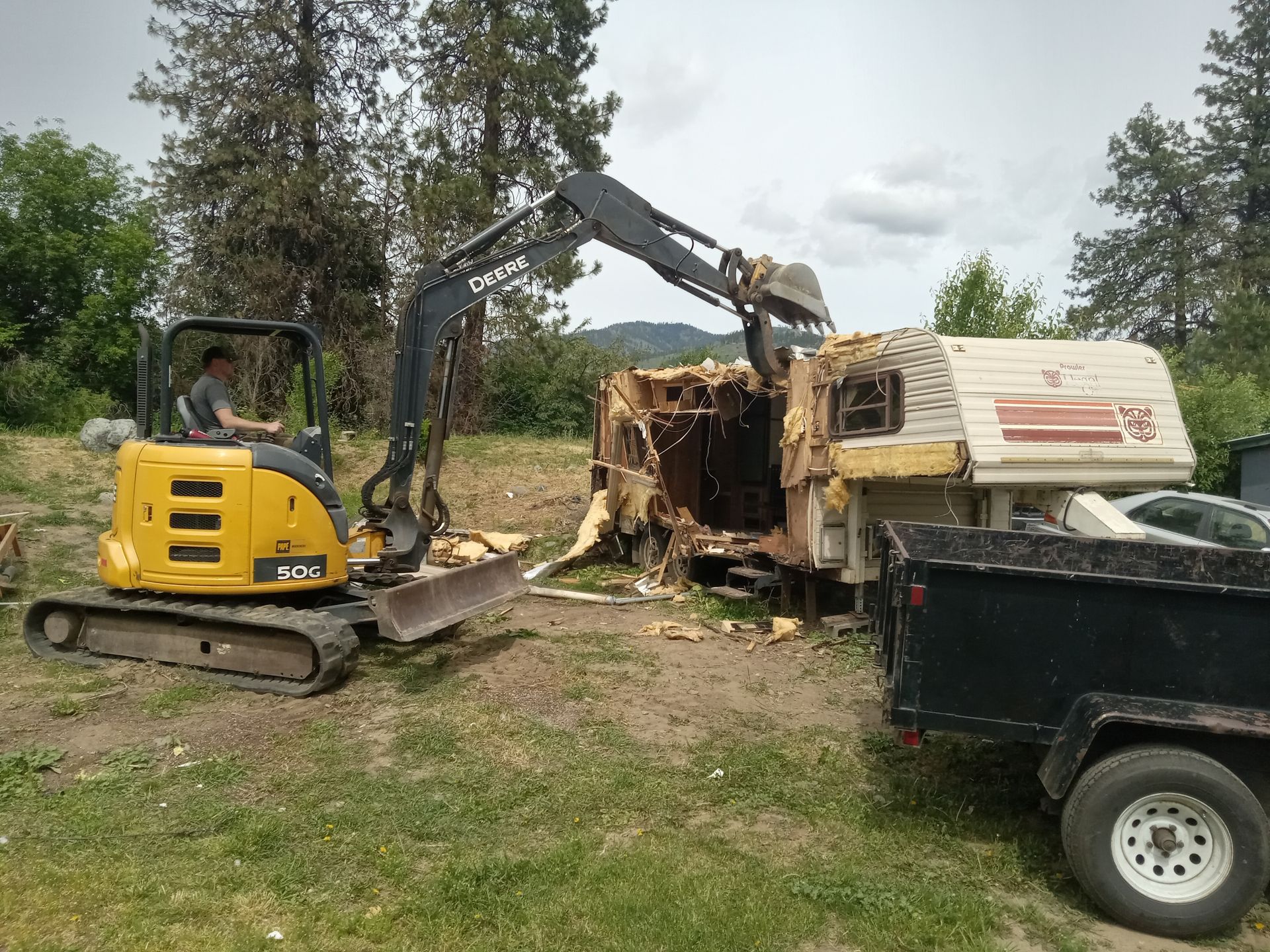 A yellow excavator is demolishing a trailer in a field.