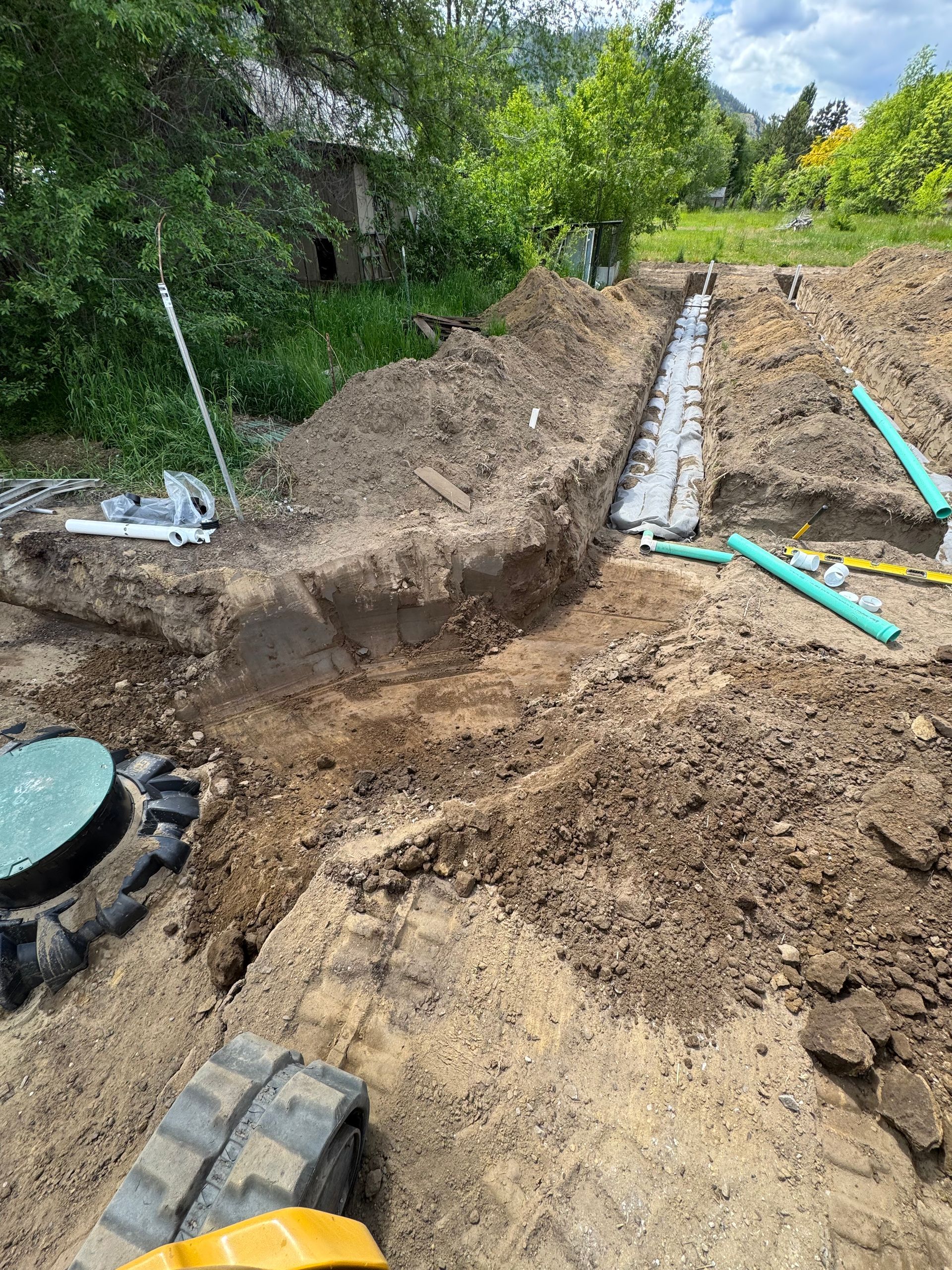 A tractor is digging a hole in the dirt next to a septic tank.