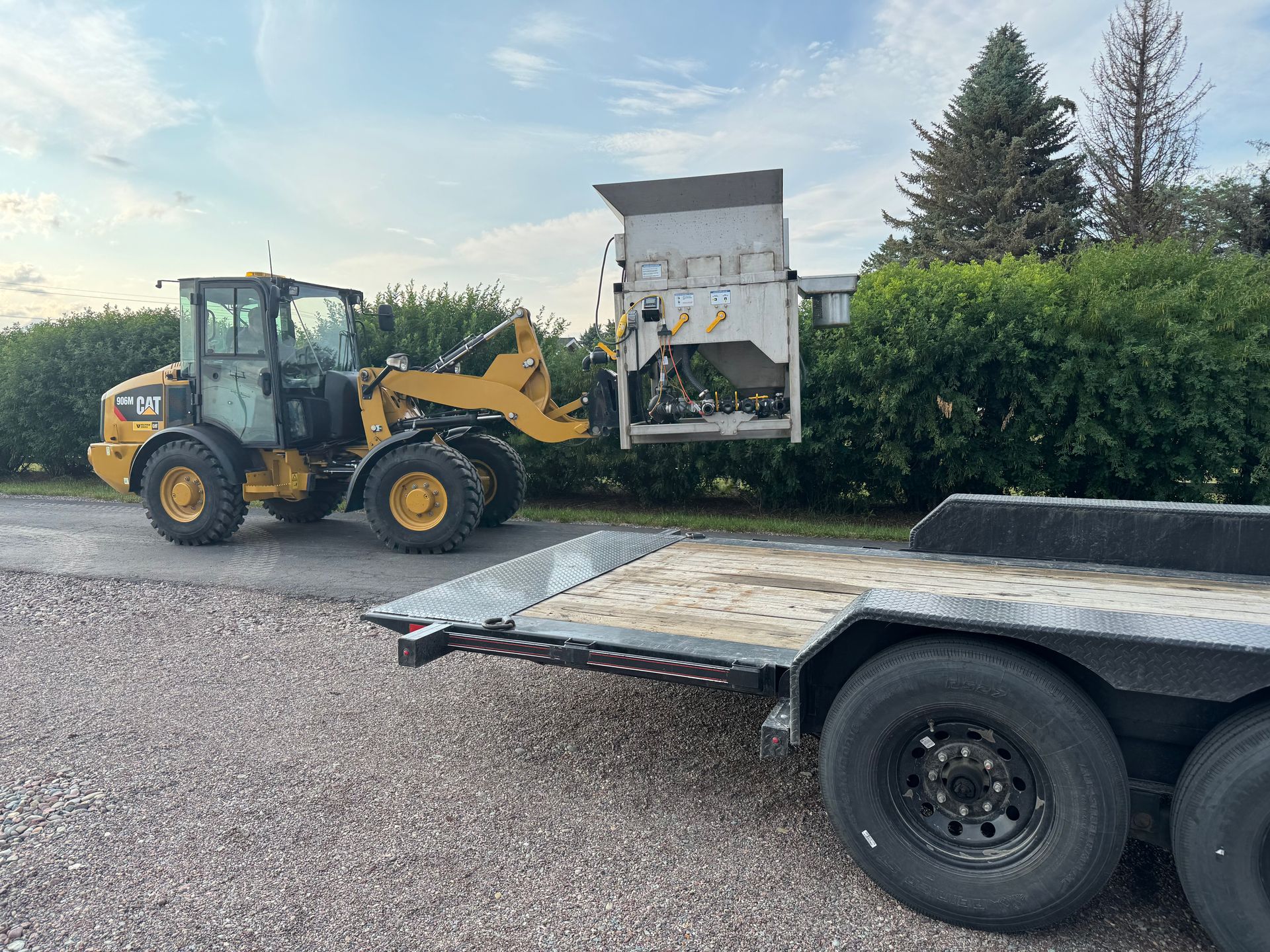A bulldozer is parked next to a trailer on a gravel road.