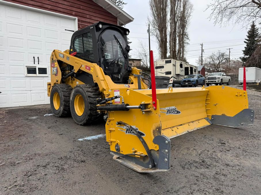 A yellow snow plow is parked in front of a garage.