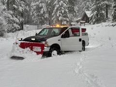 A snow plow is driving through the snow on a snowy road.