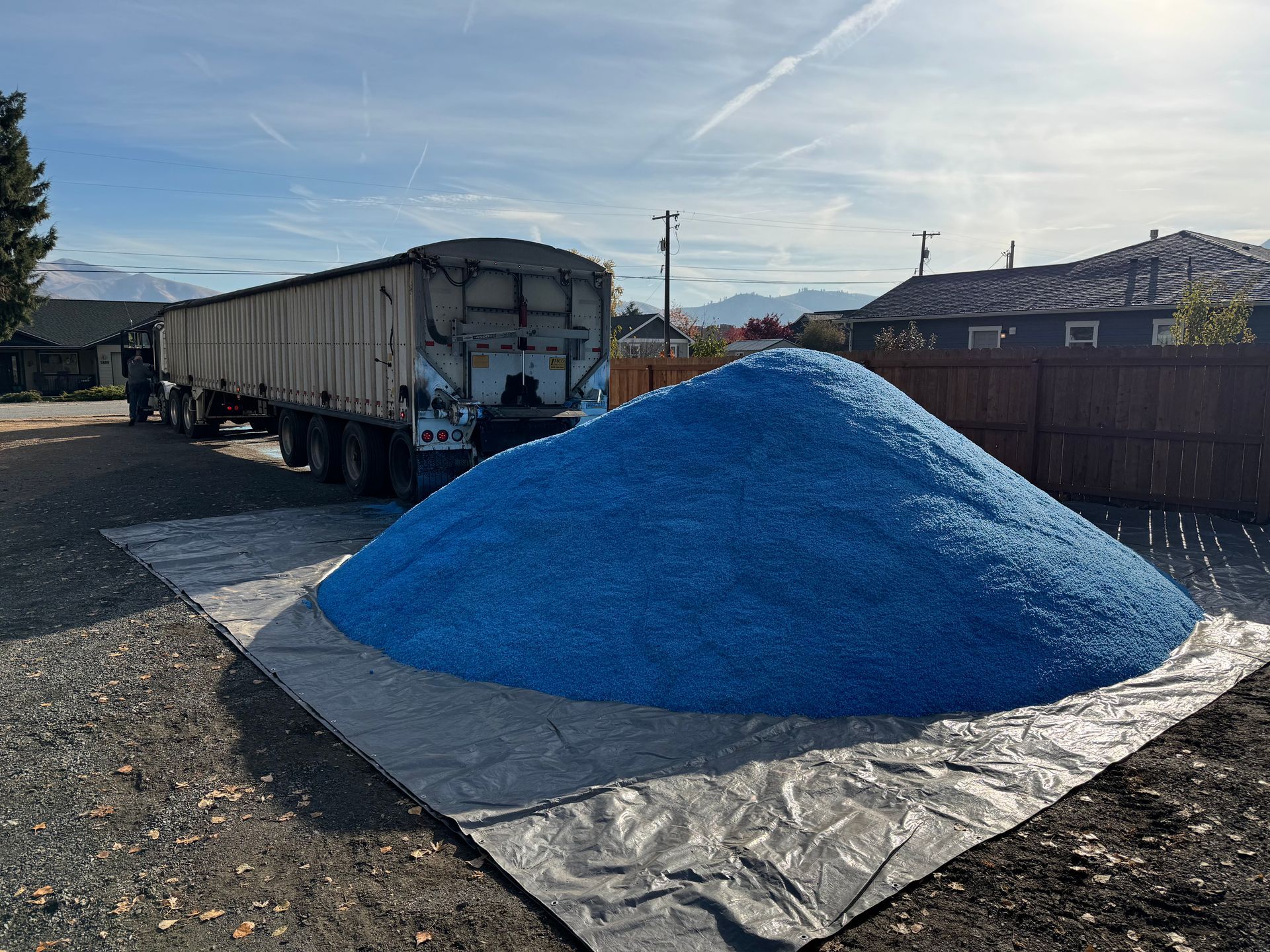 A large pile of blue gravel is sitting on a tarp next to a truck.