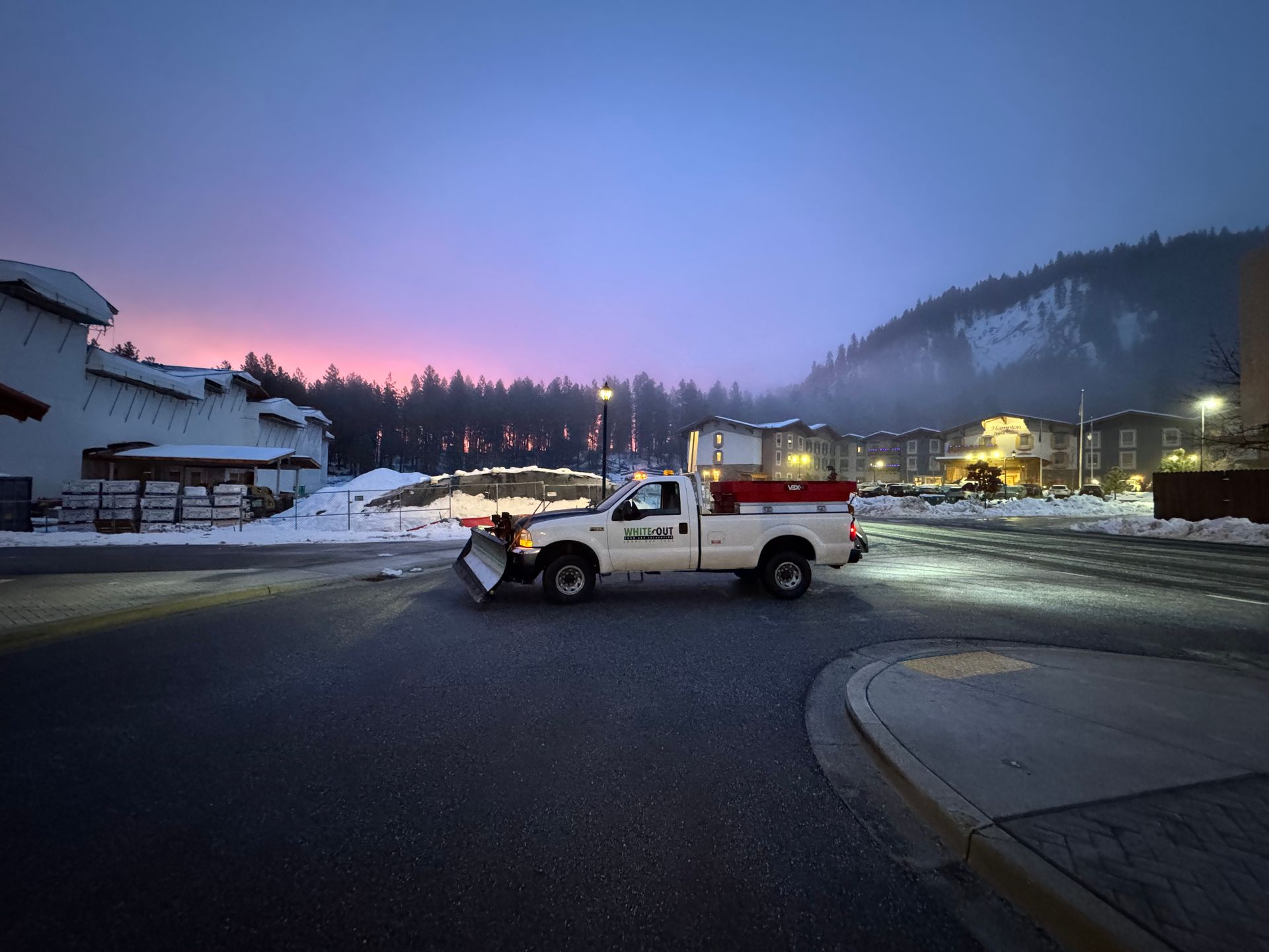 A snow plow is driving down a street at night.